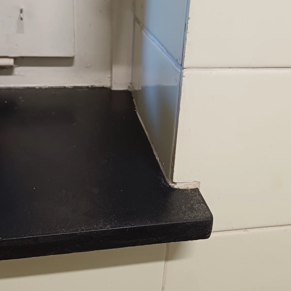 Schwarze Fensterbank in einer gefliesten Laibung, Fliesen ober- und unterhalb